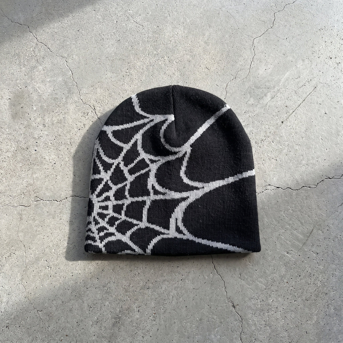 Black and ash web knit beanie laid flat, the jacquard spider web knitted into the fabric